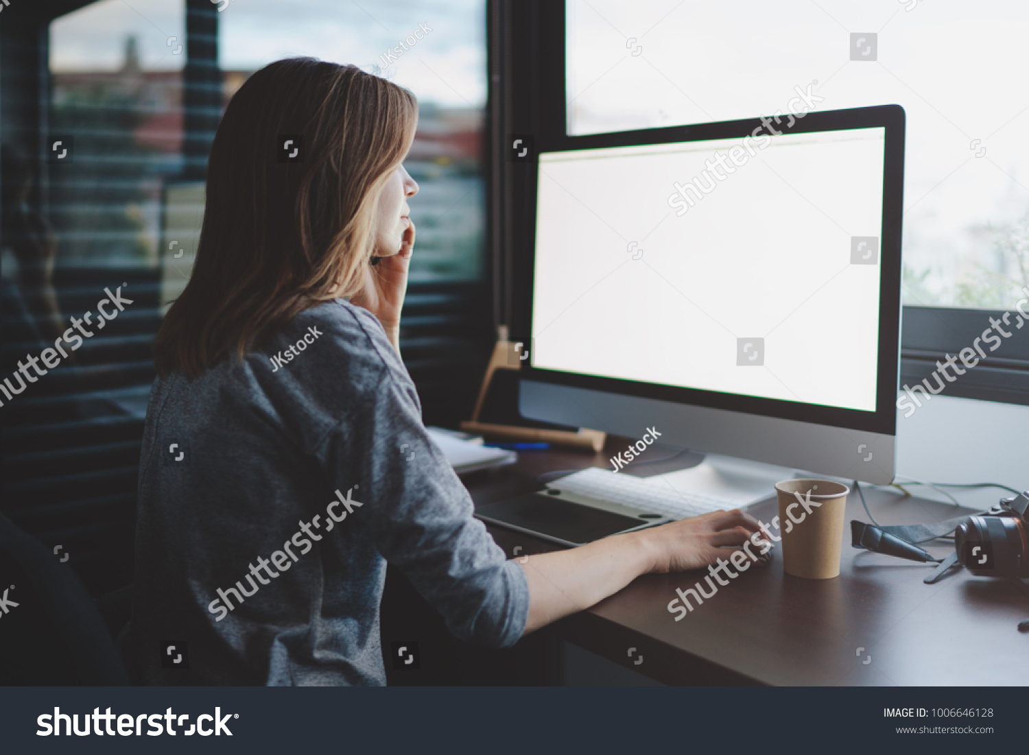 view from back to female student is talking on smartphone sitting at desk in front of monitor with blank space for design. Mockup screen with copy space. woman makes a business call