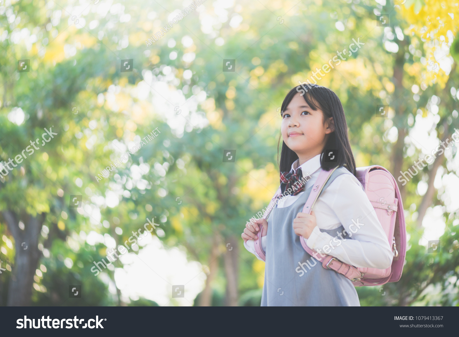 Beautiful Asian school girl with pink backpack looking up outdoors back to school concept