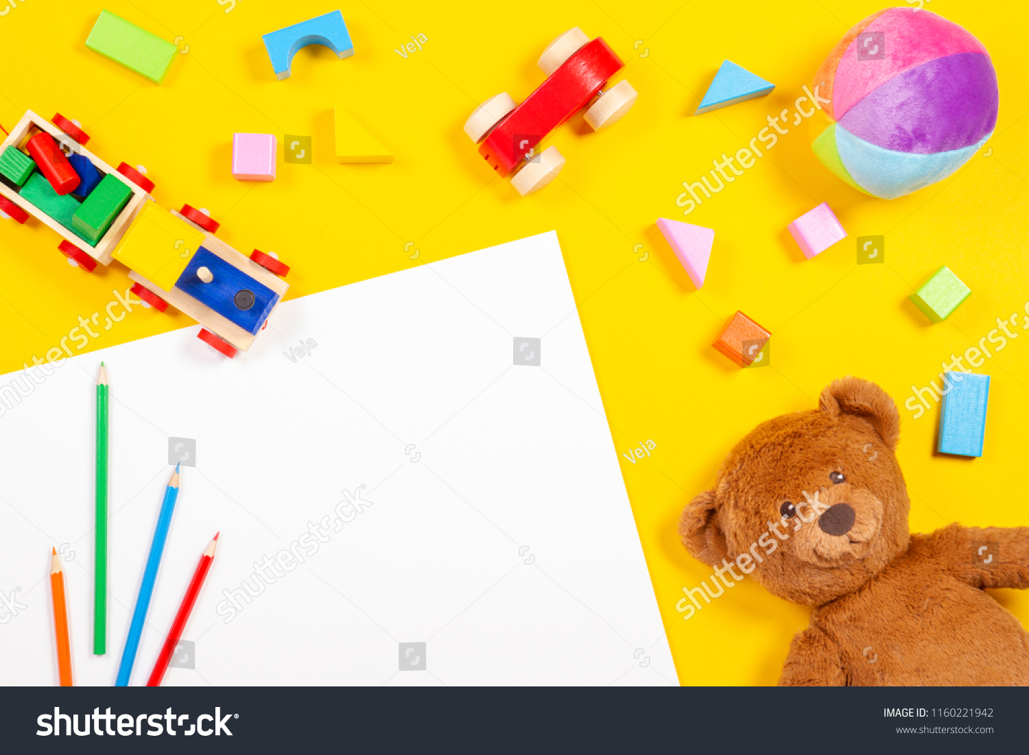 Baby kids toys background. Blank white card colored pencils wooden and soft toys on yellow background. Top view