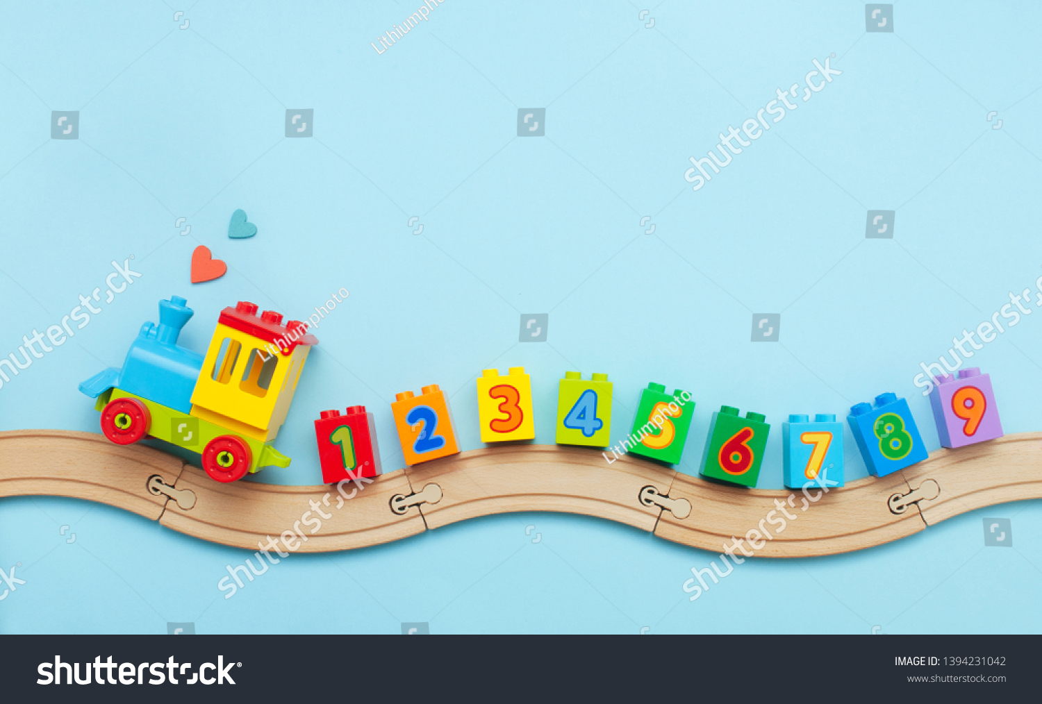 Toys background with copy space. Kids toy train with numbers on toy wooden railway on light blue background with blank space for text. Top view flat lay.