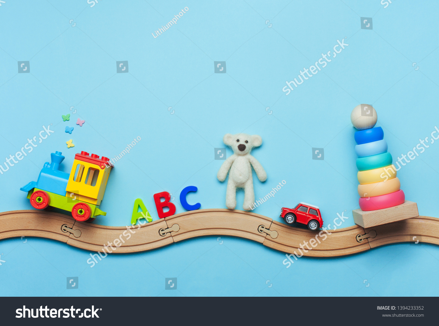 Toys background with copy space. Kids toys train ABC letters bear car and pyramid on toy wooden railway on blue background with blank space for text. Top view flat lay.