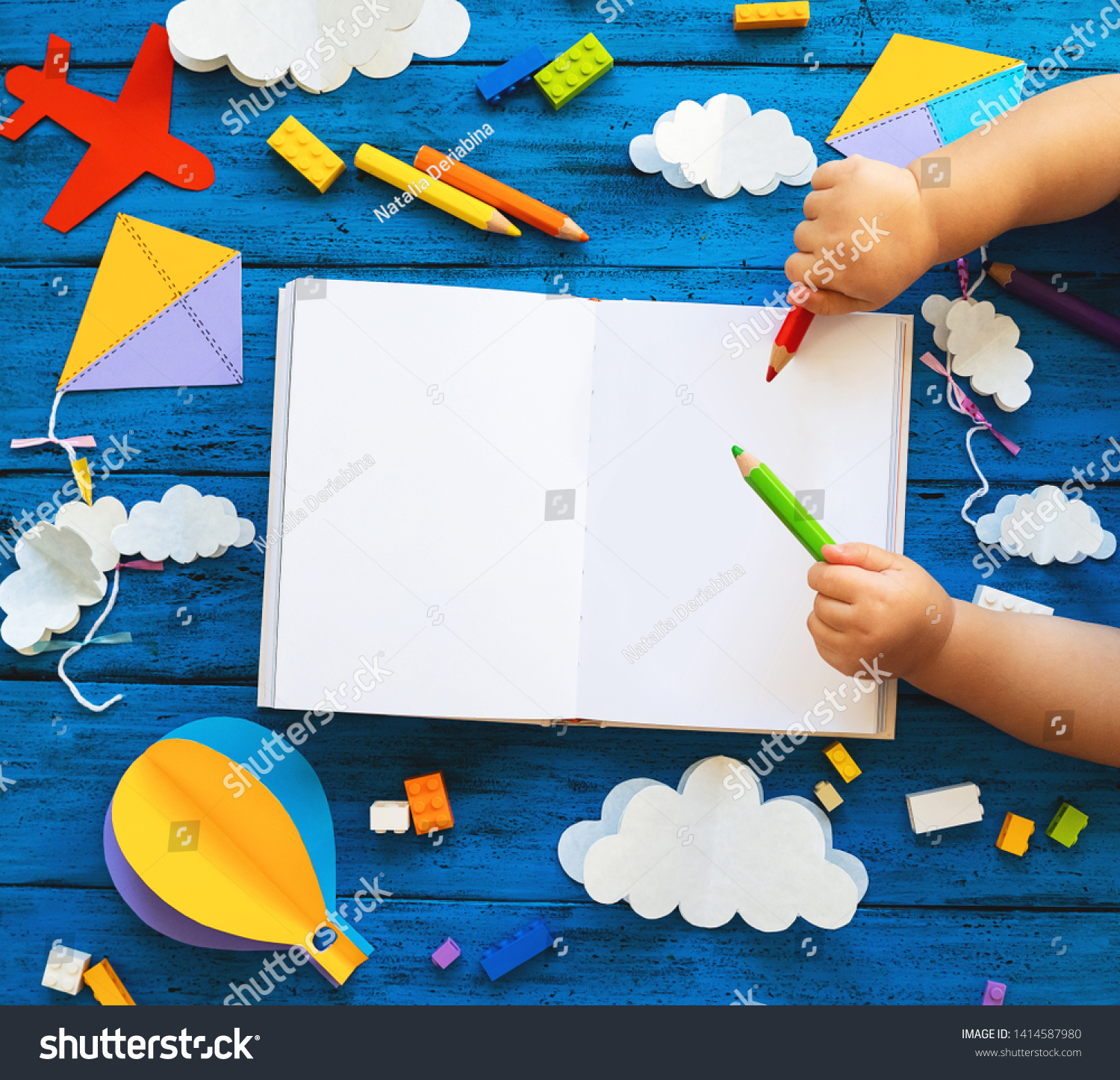 Сolourful toy bricks paper crafts and blank book with child hands on blue wood board. School or preschool creative background. Concept of DIY construction playing education or learning languages