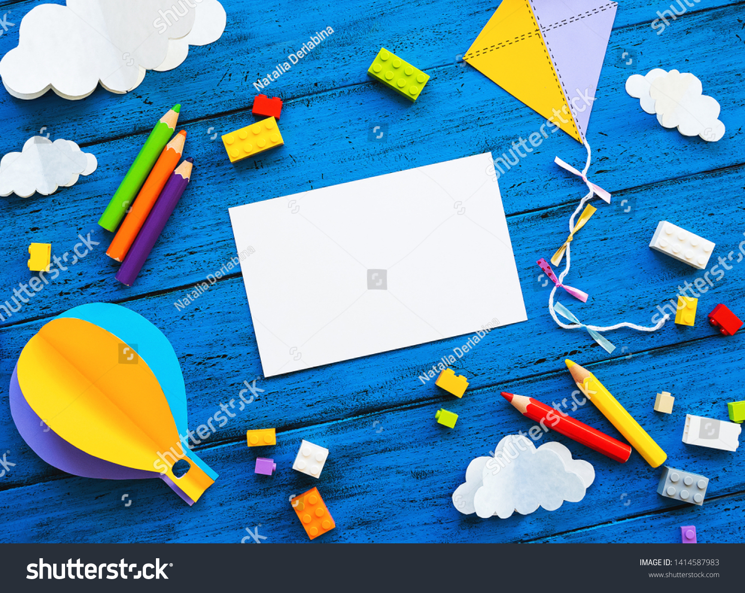 Сolourful toy bricks paper crafts and blank card on blue wood board. School or preschool creative background. Concept of DIY construction adventure playing child education or kids learn languages