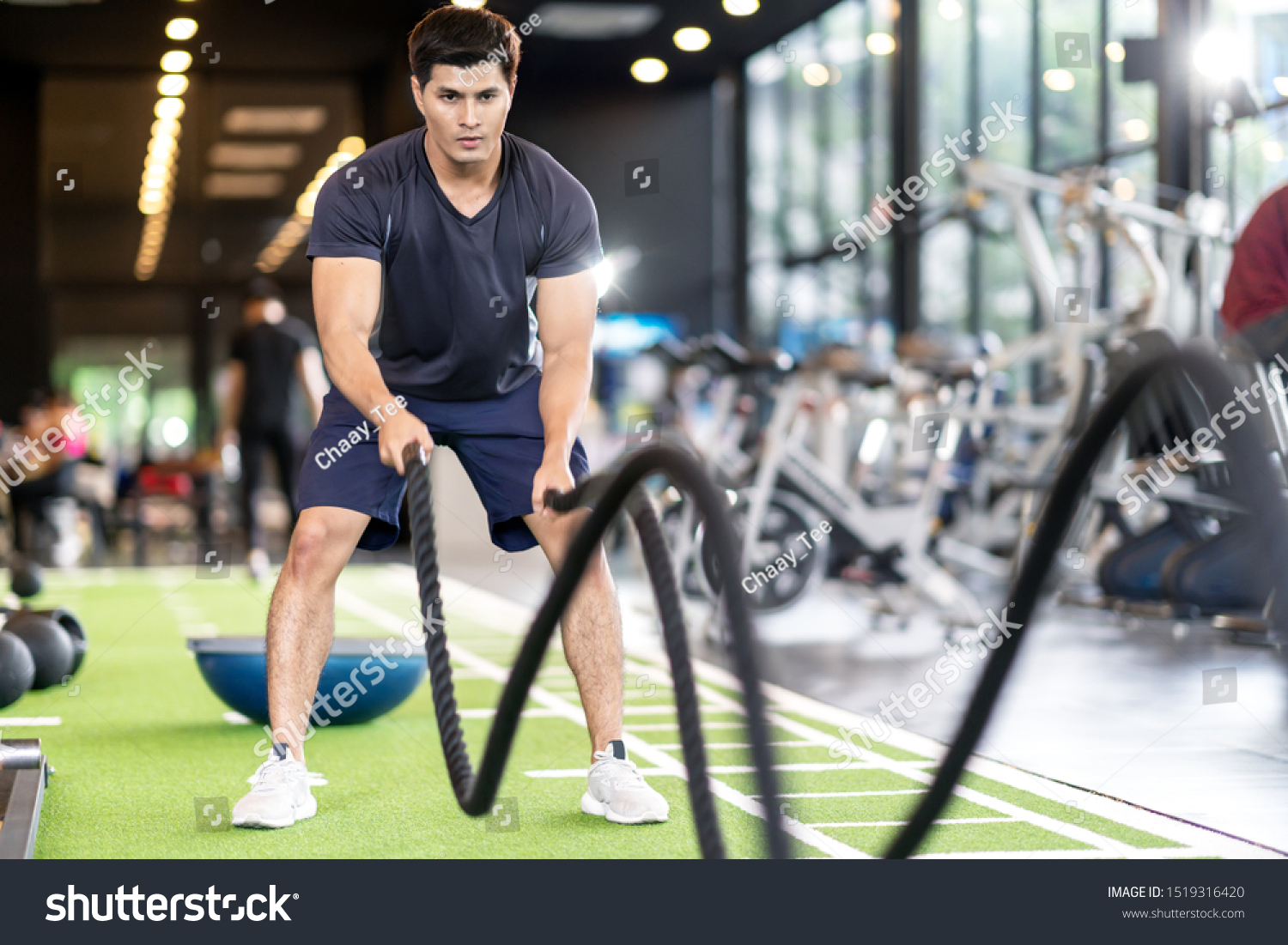 Sporty asian man exercising with battle ropes at the gym on green floor. Strong male determine with her indoor workout for stamina and building muscular body. Athlete battle rope workout concept.