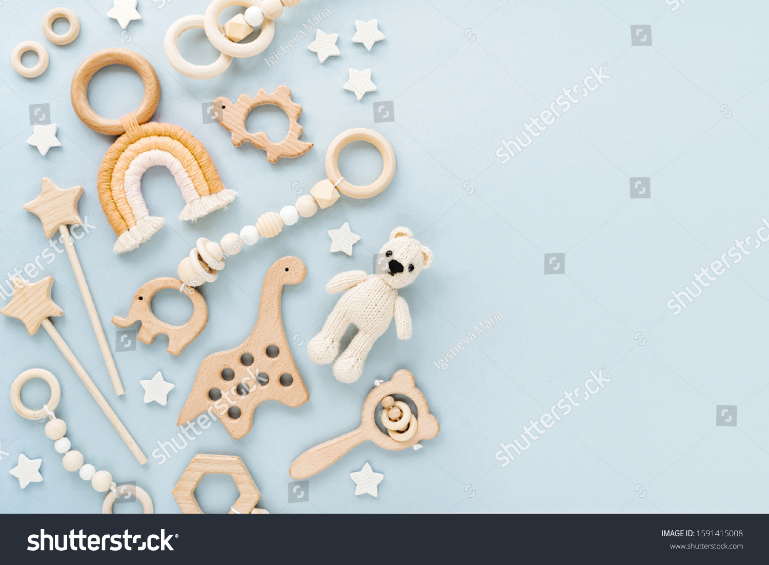 Cute wooden baby toys on light-blue background. Knitted bear rainbow dinosaur toy beads and stars. Eco accessories beanbag and teethers for newborn. Blank space for text. Flat lay top view