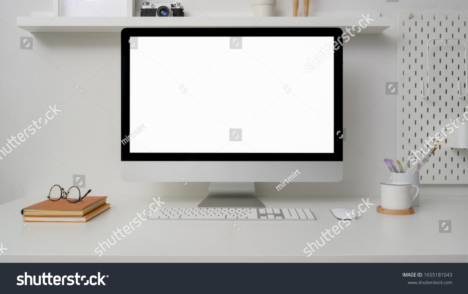 Close up view of minimal workspace with blank screen computer office supplies and decorations on white desk with shelf on white wall