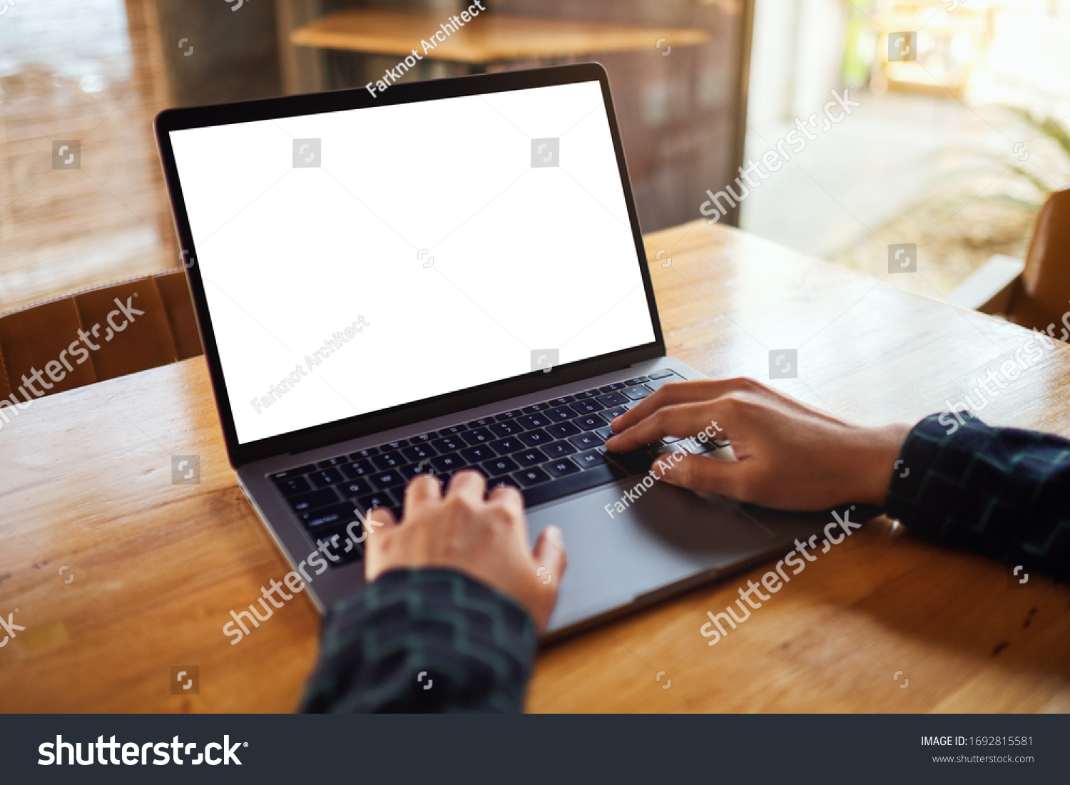Mockup image of a woman using and typing on laptop computer with blank white desktop screen on wooden table