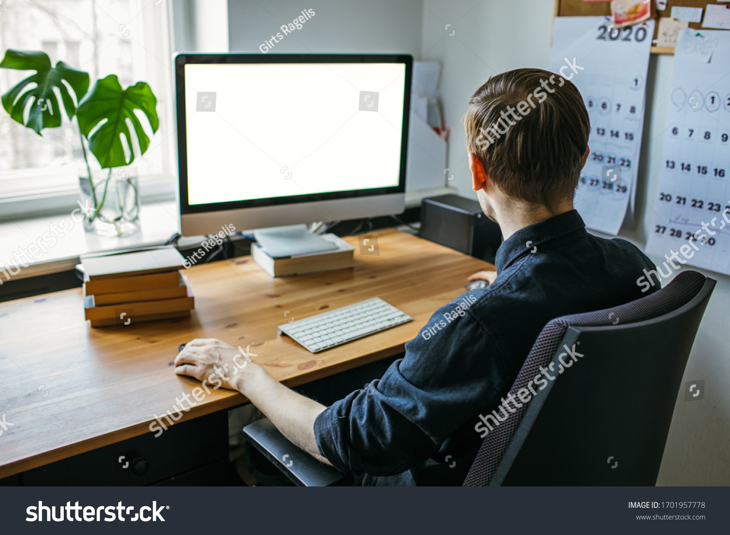 Man working from home office. Computer with blank empty screen for copy space and information. Businessman from behind shoulder view. A creative entrepreneur