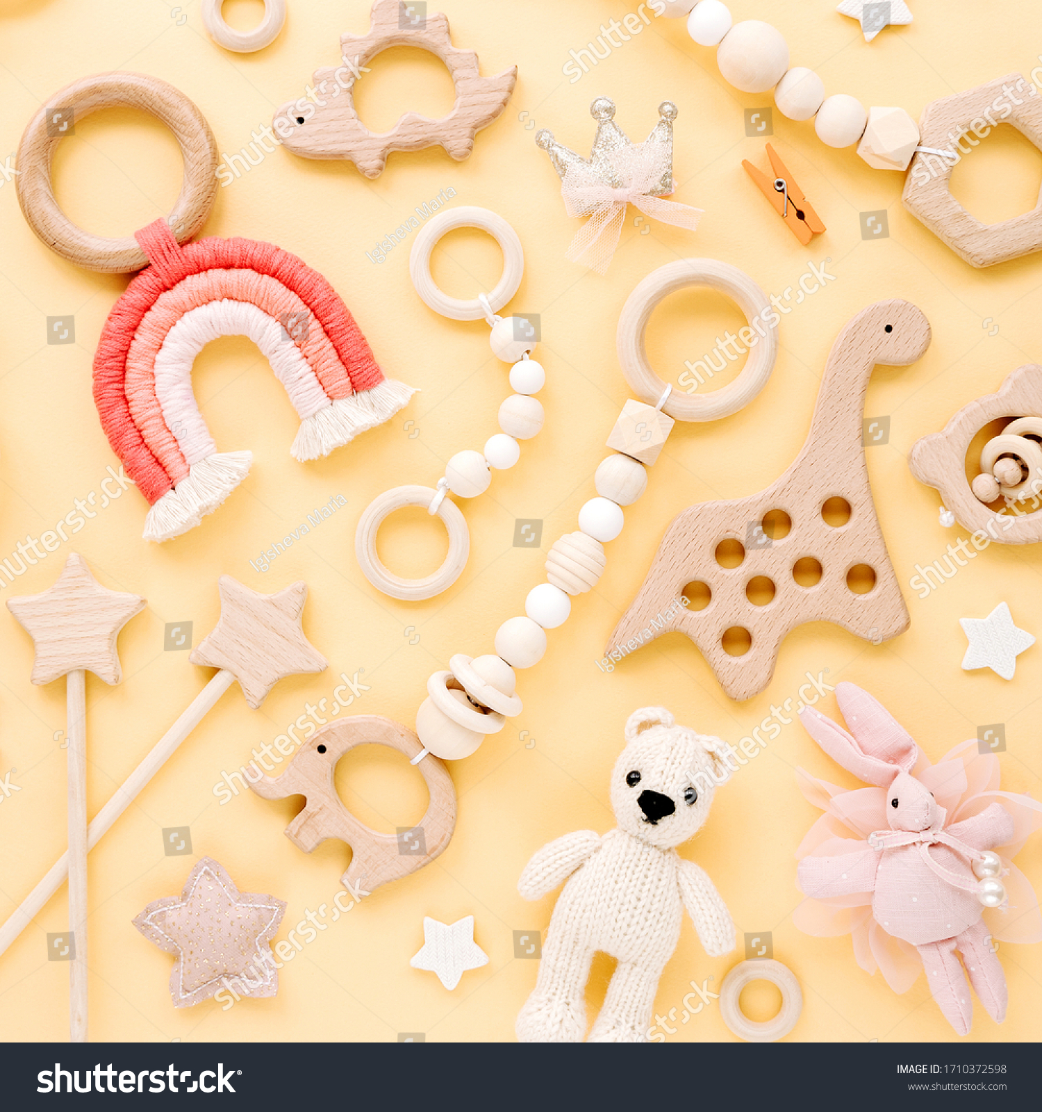 Cute wooden baby toys on yellow background. Knitted bear rainbow dinosaur toy beads and stars. Eco accessories beanbag and teethers for newborn. Flat lay top view