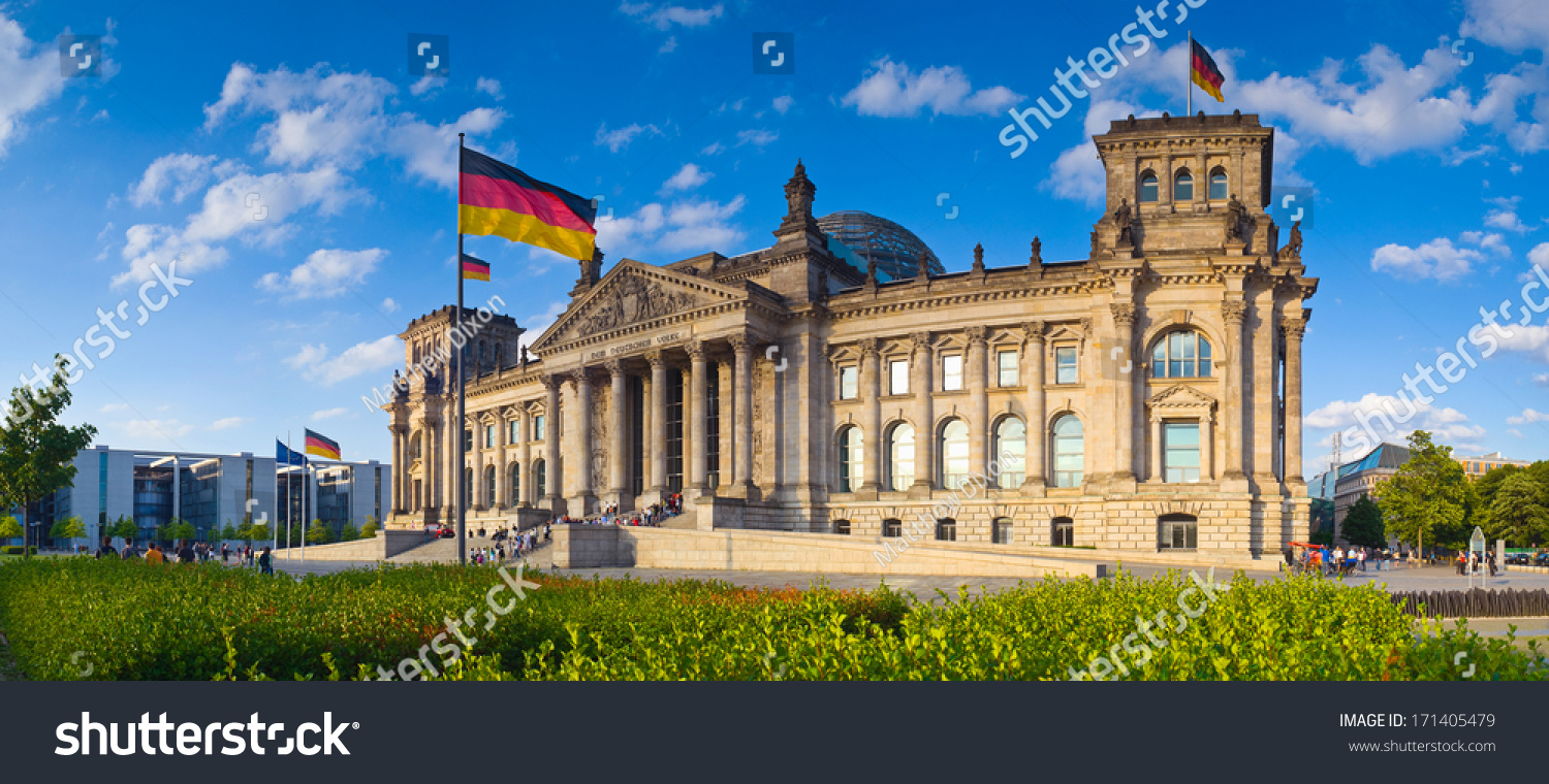 Warm evening sunlight illuminating the mighty Reichstag parliament (1894) with clear blue sky and flags flying.