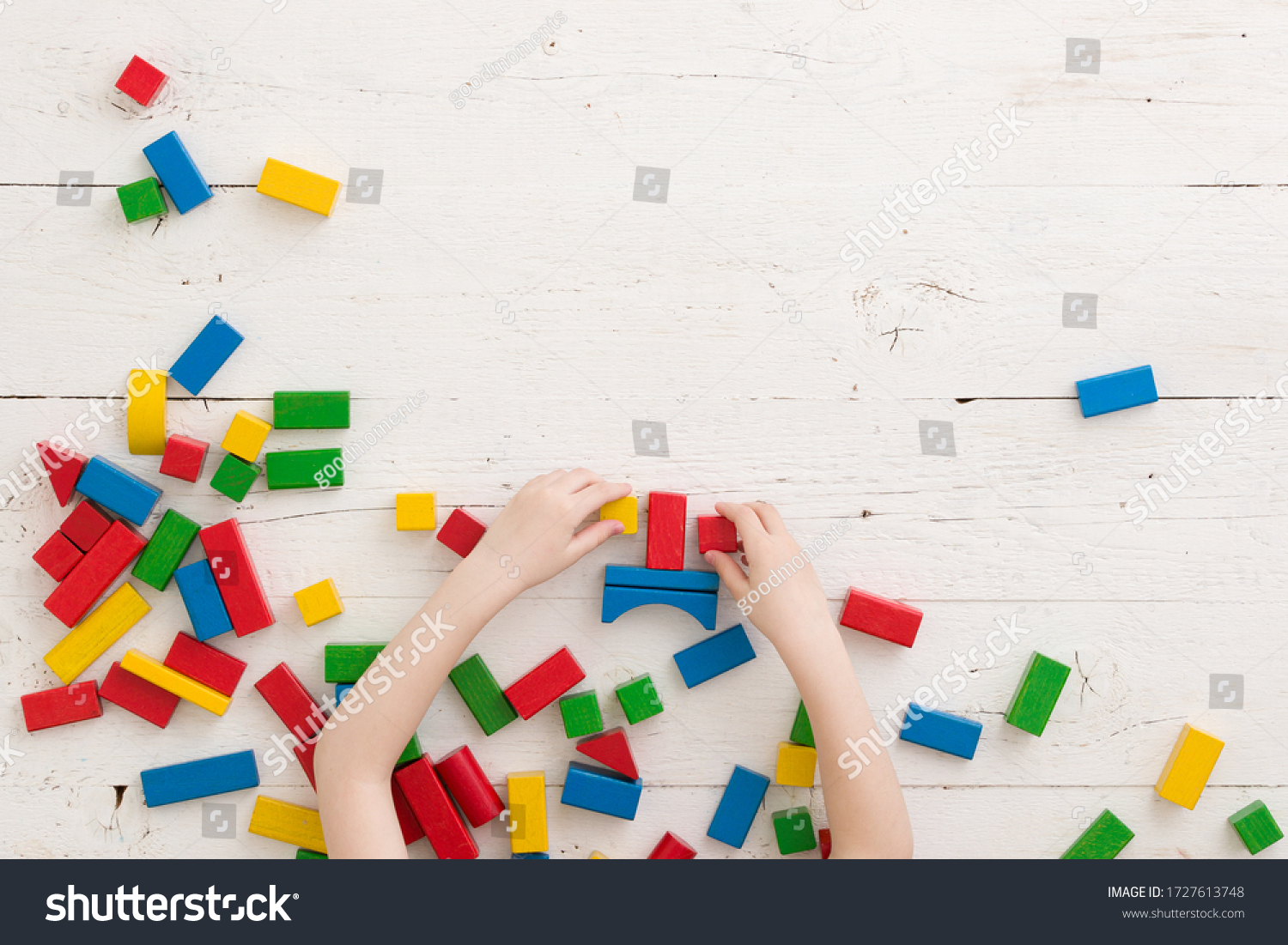 Baby boy or girl play with colorful bricks on a white wooden table. Top view on wooden colorful bricks on a wooden background. School education and learning concept.