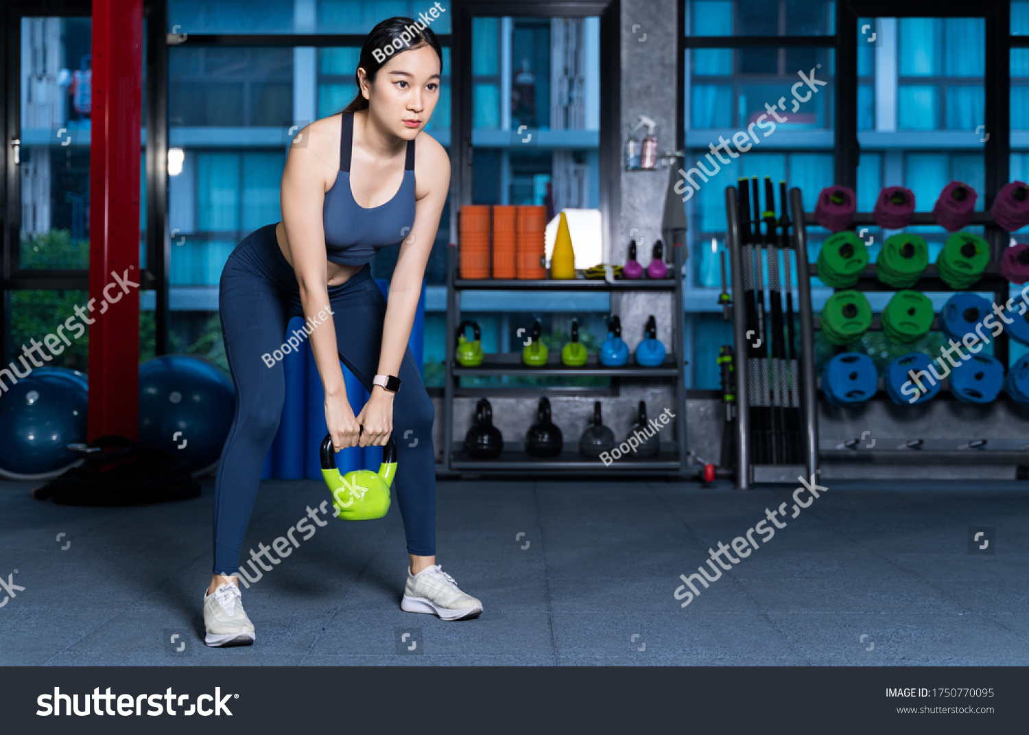 Healthy asian women are doing lifting gear she's doing weight training exercises with Kettlebell at the fitness or gym with blur Racks Fitness Equipment background in sport and healthy concept