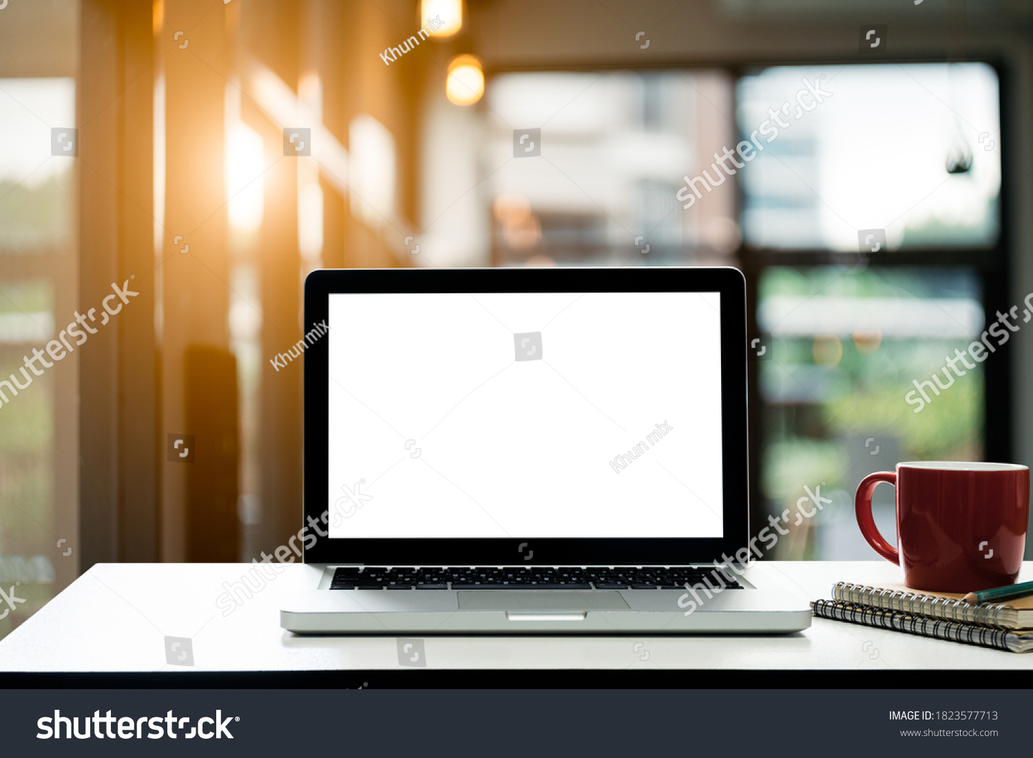 Conceptual workspace Laptop computer with blank white screen and notebook and coffee cup on table in loft restaurant blurred background.