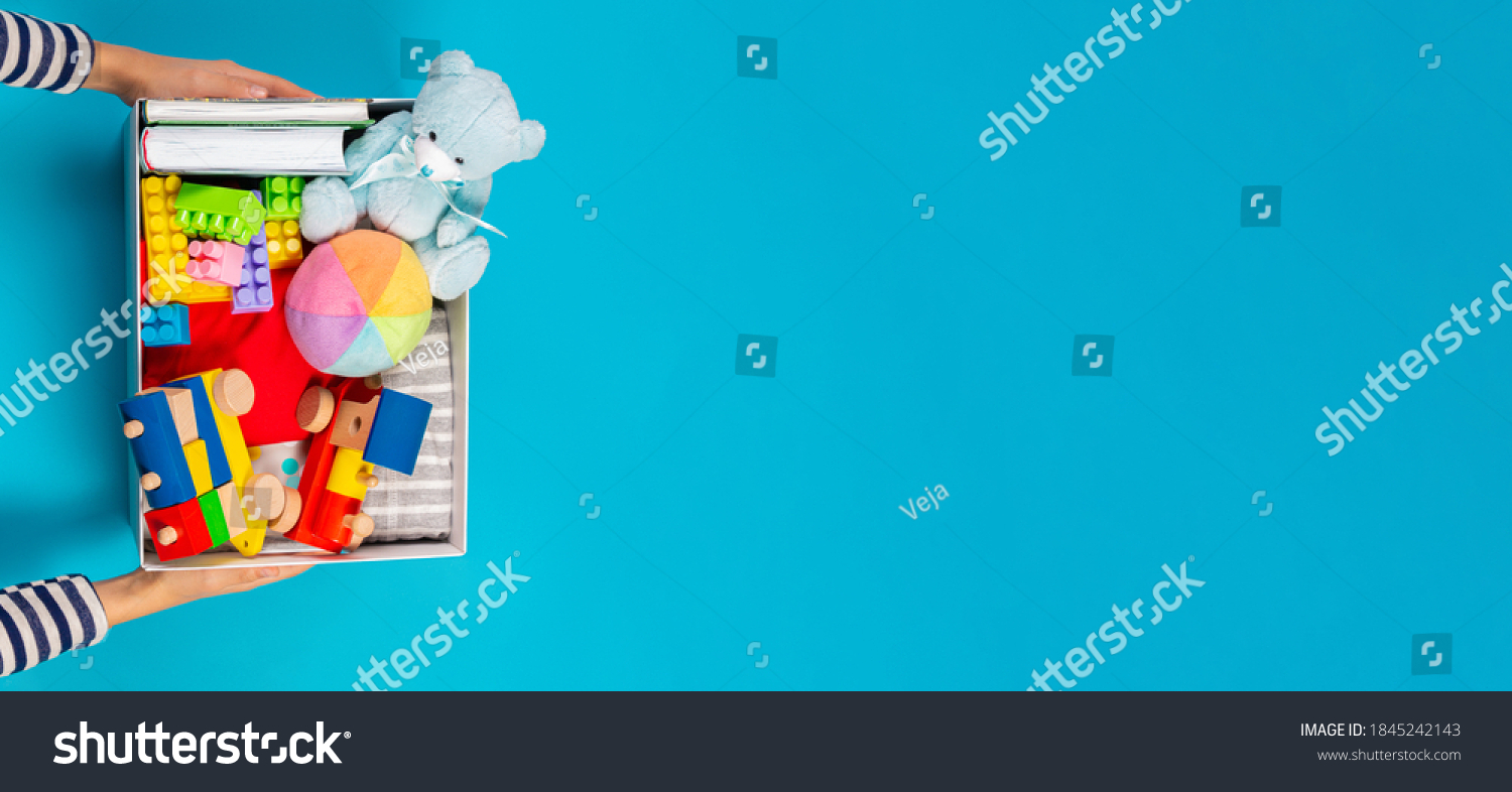 Donation concept. Kid hands with donate box with clothes books and toys on light blue background. Top view