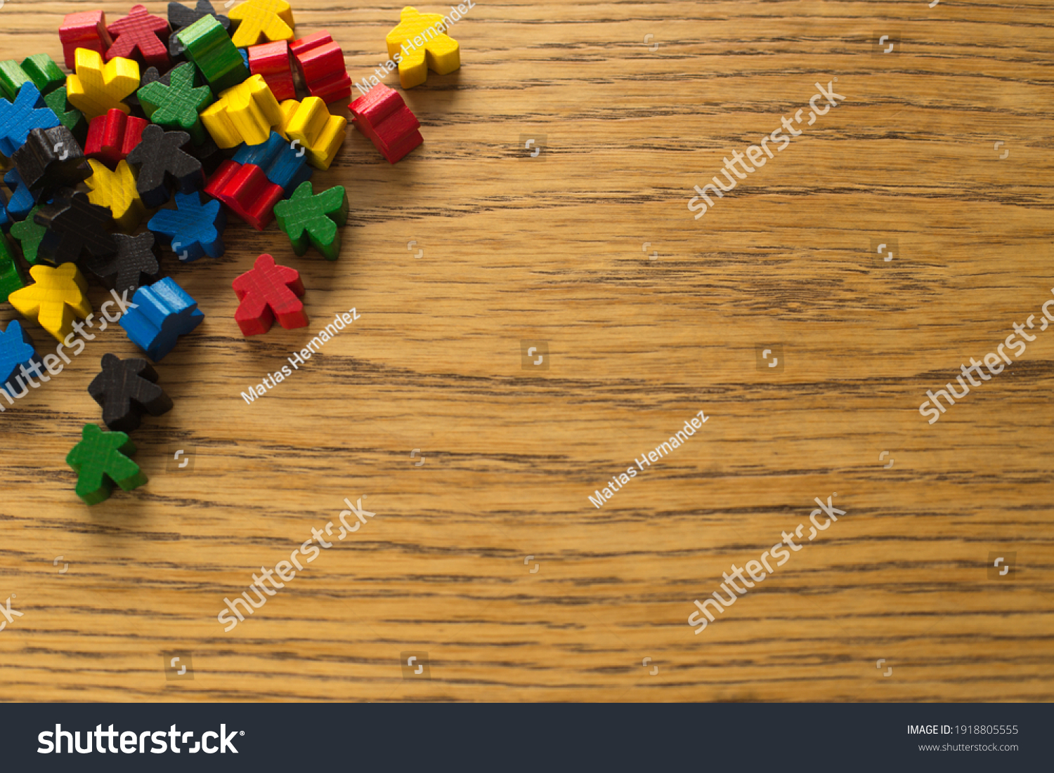 Colorful meeple on wooden background. Board game concept. Diversity of people and colors. The chips are out of order on the table.