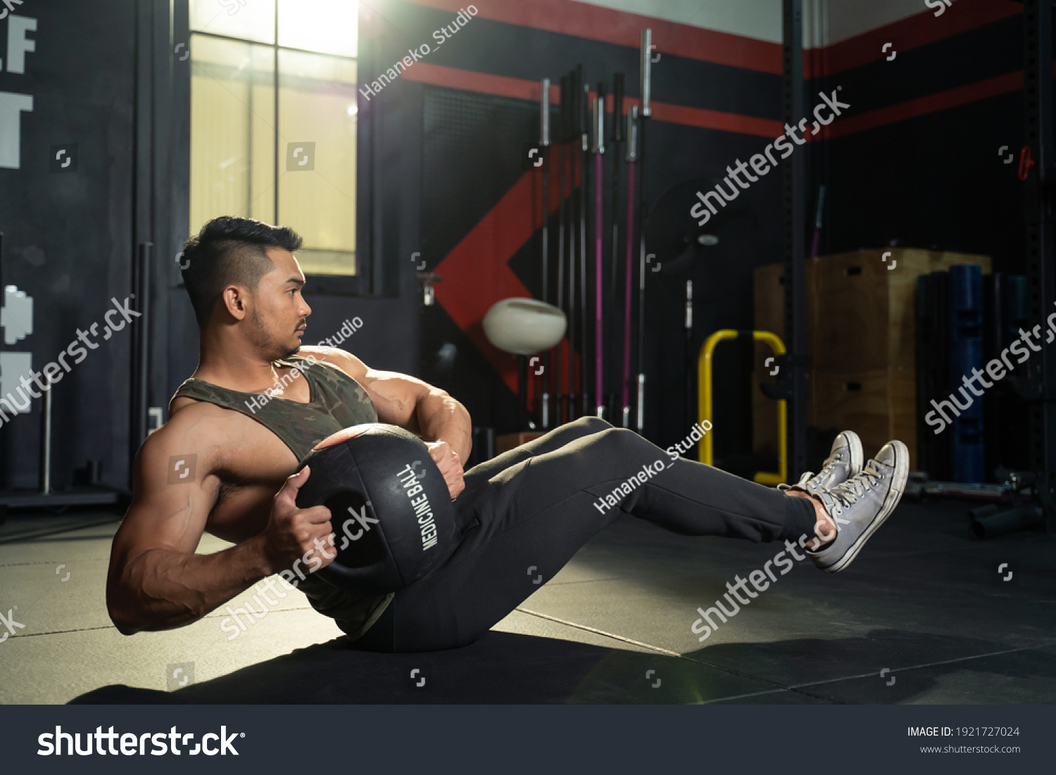 Working out at GYM concept. Young Asian handsome man working out his abdominal muscles by holding the medicine twist left and right sitting in the modern loft gym. Health and fitness concept.