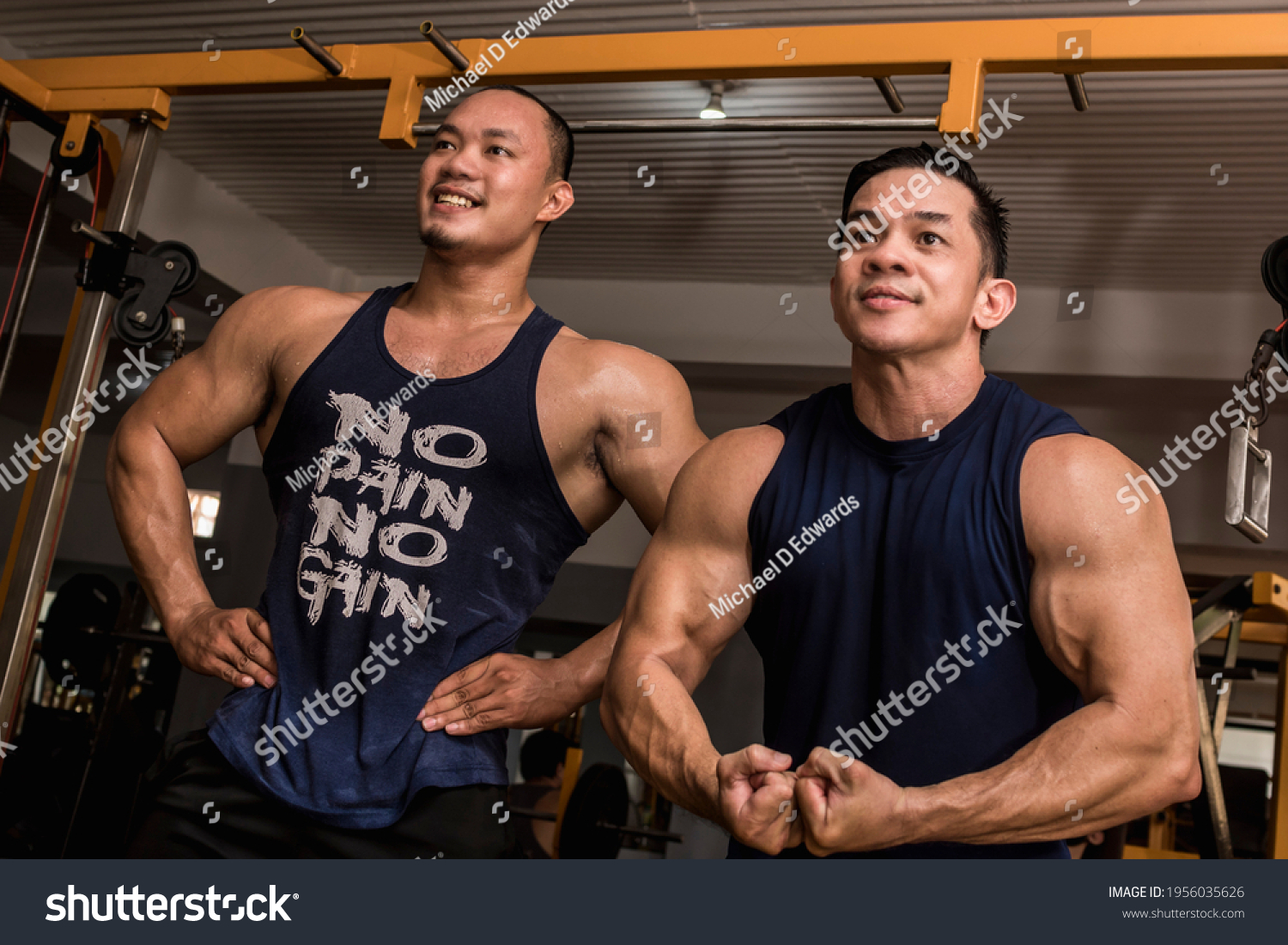 Two friends enjoy a friendly posedown after training doing standing relaxed and most muscular poses. Having fun and camaraderie at the gym.