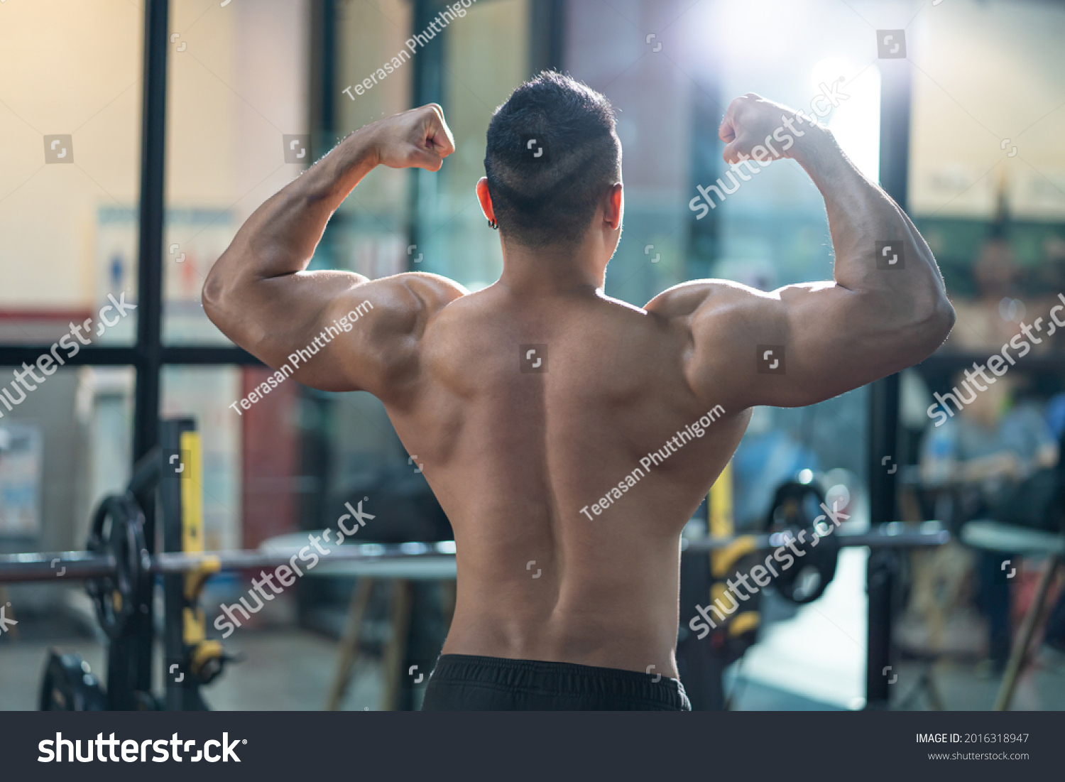 Unidentified shirtless adult Asian men sweating while lift up the barbell workout machine for muscle part inside of fitness gym. Bodybuilding athlete sport training for body strength and good health.