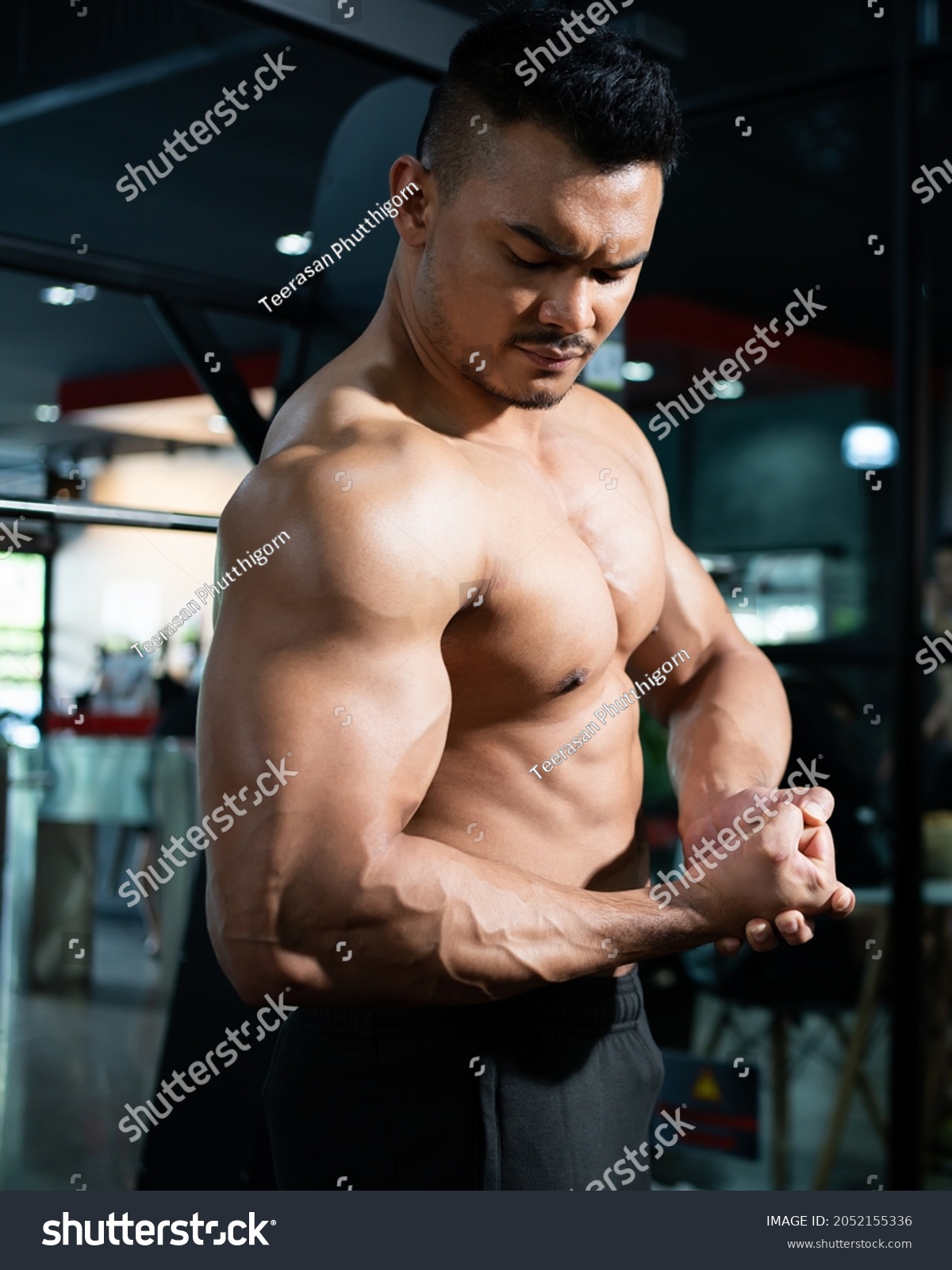 Portrait shot of shirtless adult Asian men show off his strong bicep and arm muscle inside of fitness gym. Bodybuilding or professional athlete workout concep.t