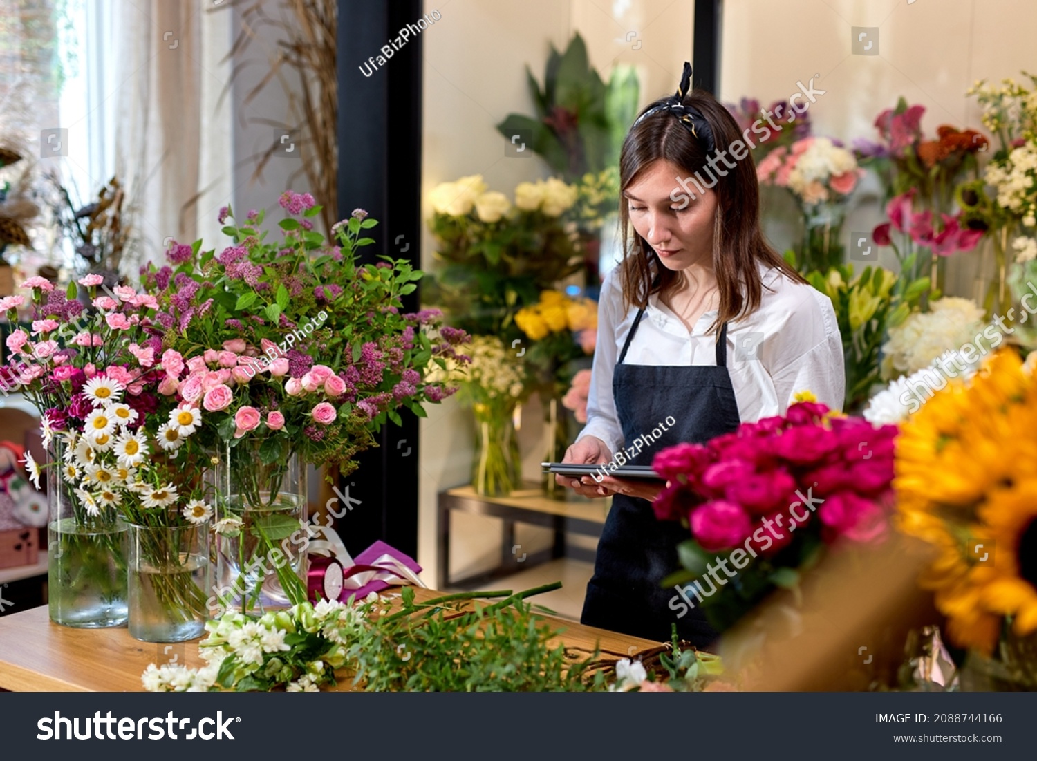business technology sale and floristry and concept. florist woman with tablet pc computer at flower shop counter. young nice florist using digital tablet Checking Personal Planer. side view