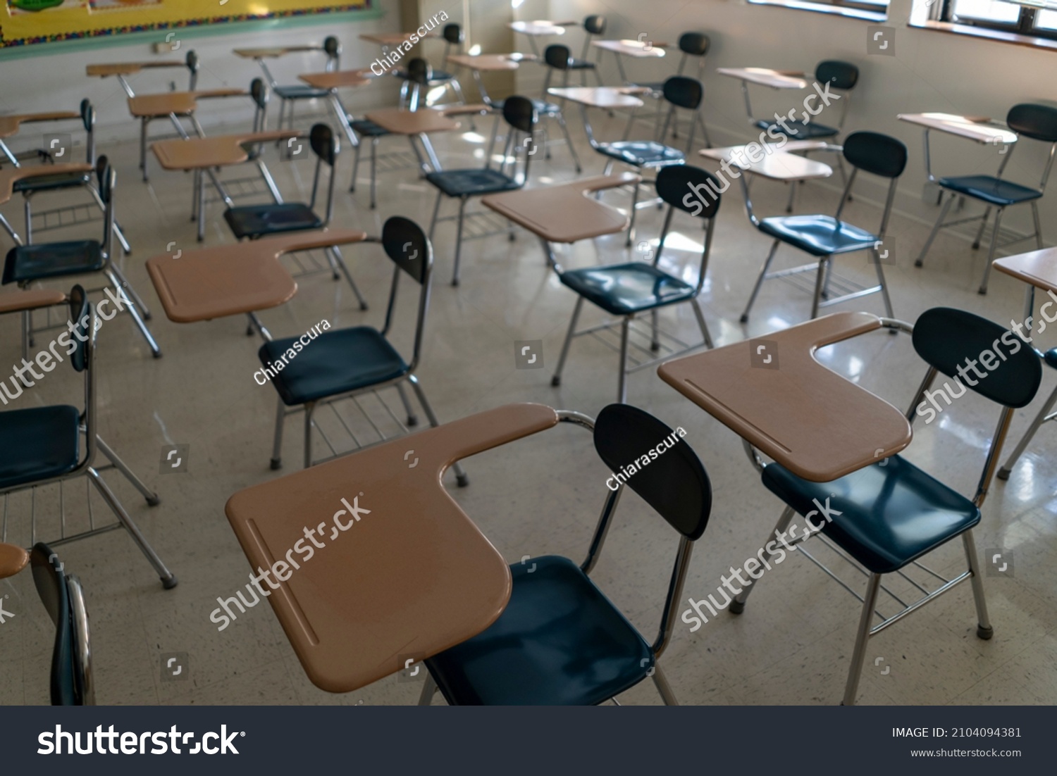 Desks in empty dark high middle or elementary school classroom with light coming through windows.