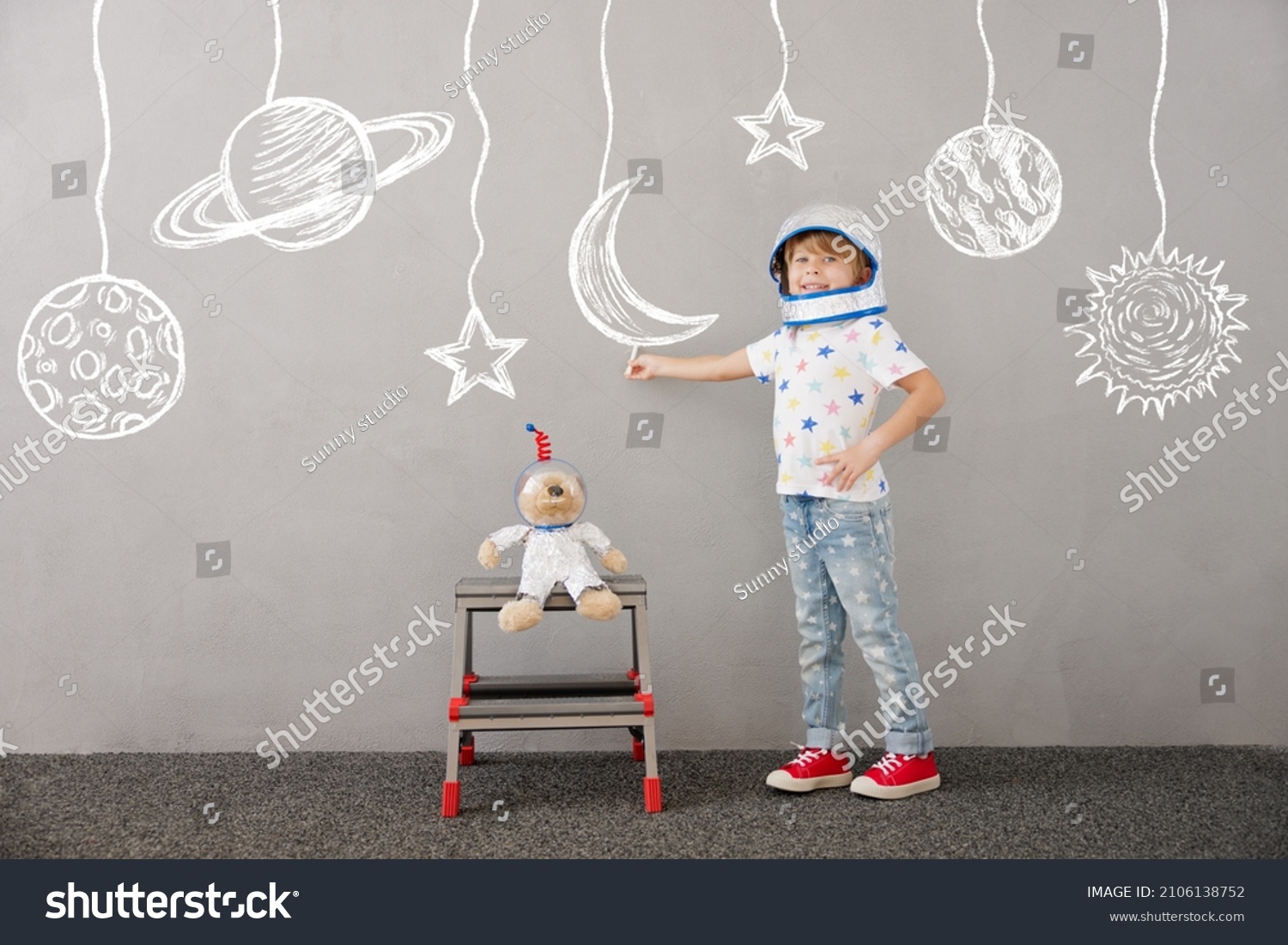 Happy child playing with teddy bear at home. Kid pretend to be astronaut. Imagination and children dream concept