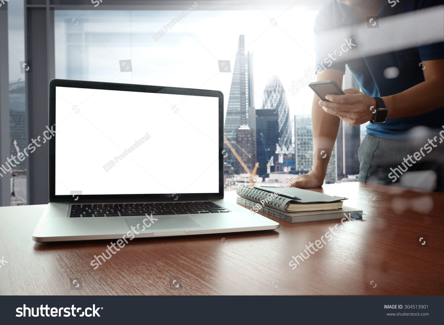 designer hand working and smart phone and blank screen laptop on wooden desk in office with london city background