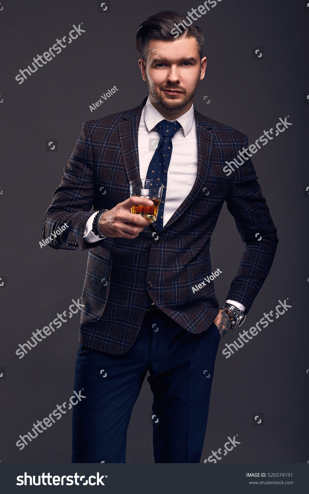 Portrait of elegant brutal man in a expensive wool suit with glass of whiskey on a gray background