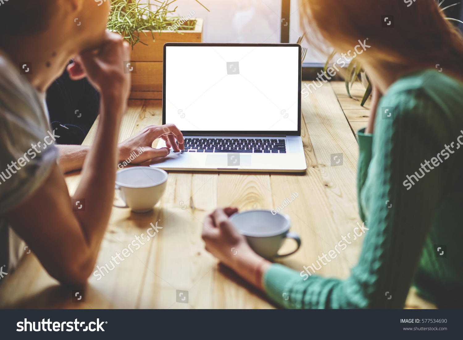 Rear view shot of hipster man keyboarding for search information in internet by using net-book. Female person look on blank mock up screen of laptop computer. Friends having coffee during recreation
