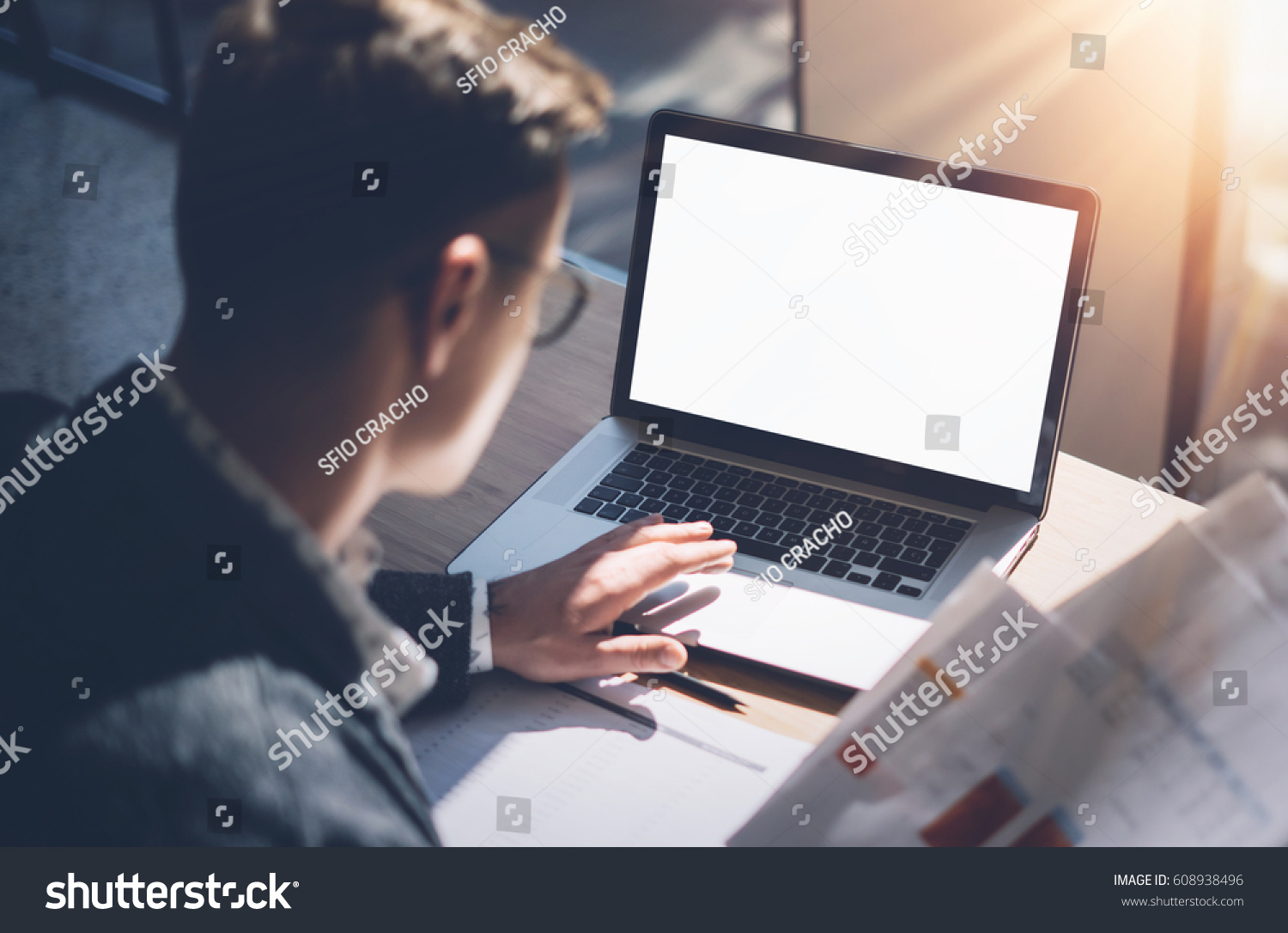 Closeup view of banking finance analyst in eyeglasses working at sunny office on laptop while sitting at wooden table.Businessman analyze stock report on notebook screen.Blurred horizontal mockup