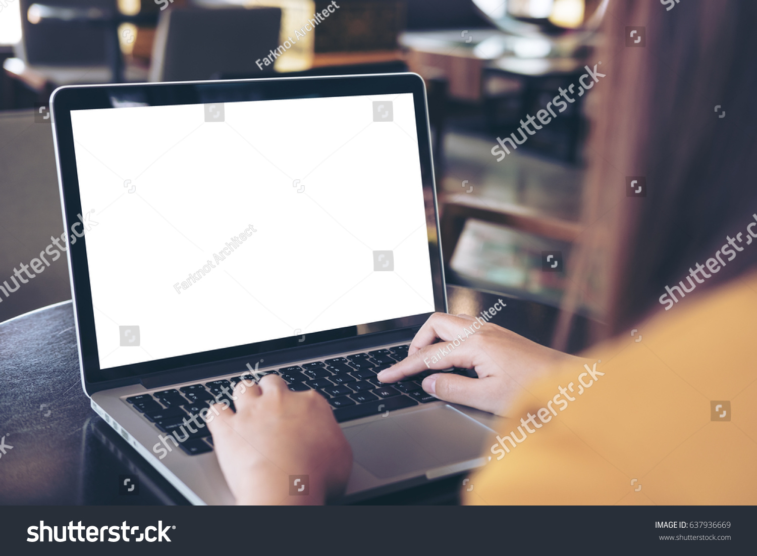 Mockup image of a woman using laptop with blank white screen on wooden table in modern cafe