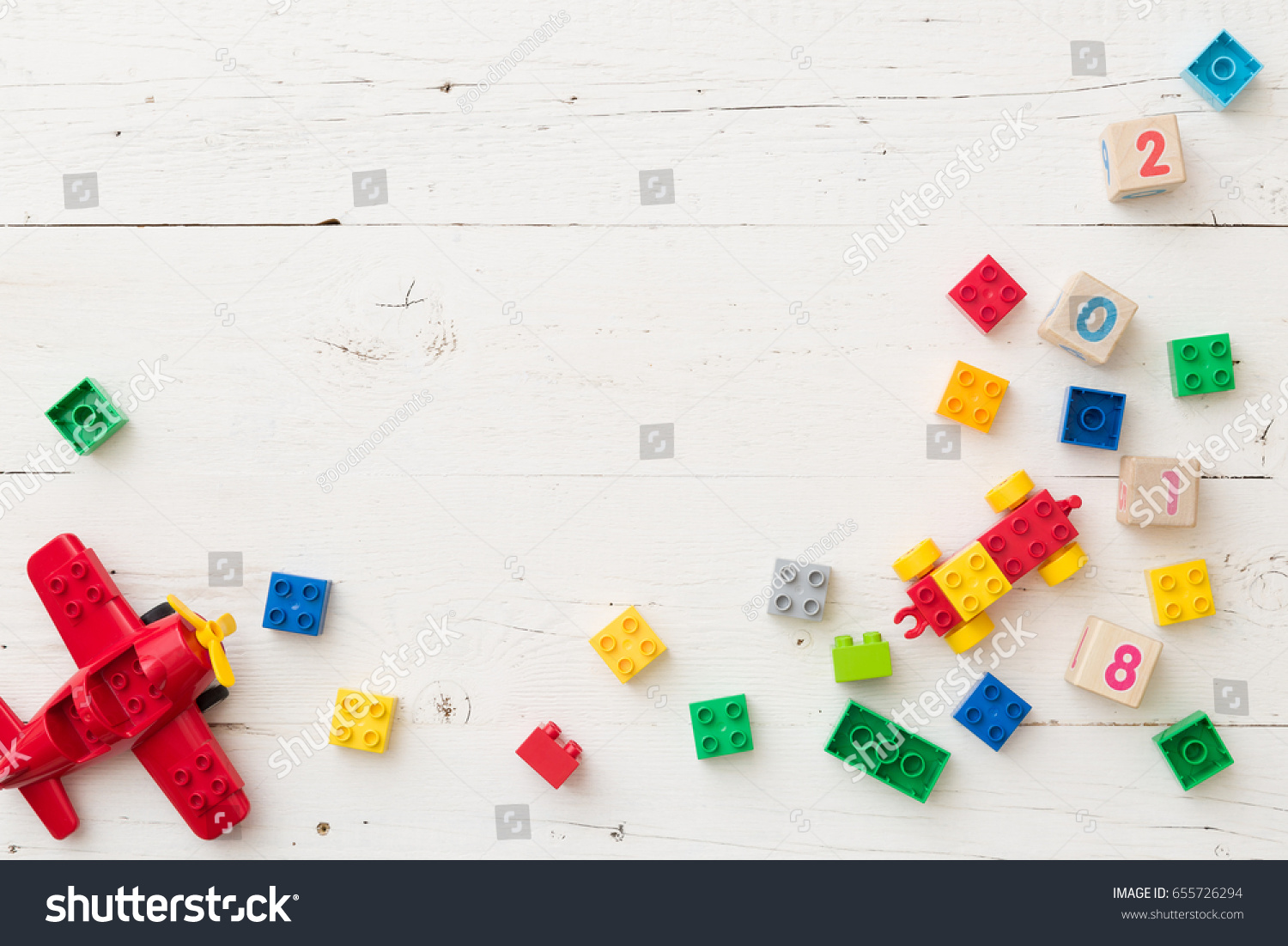 Top view on wooden cubes with numbers and colorful toy bricks and plane on white wooden background. Toys in the table