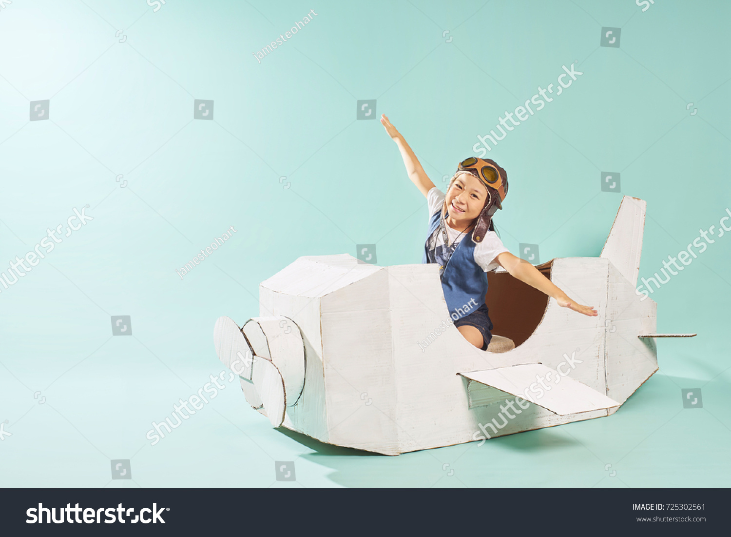 Little cute girl playing with a cardboard airplane. White retro style cardboard airplane on mint green background . Childhood dream imagination concept .