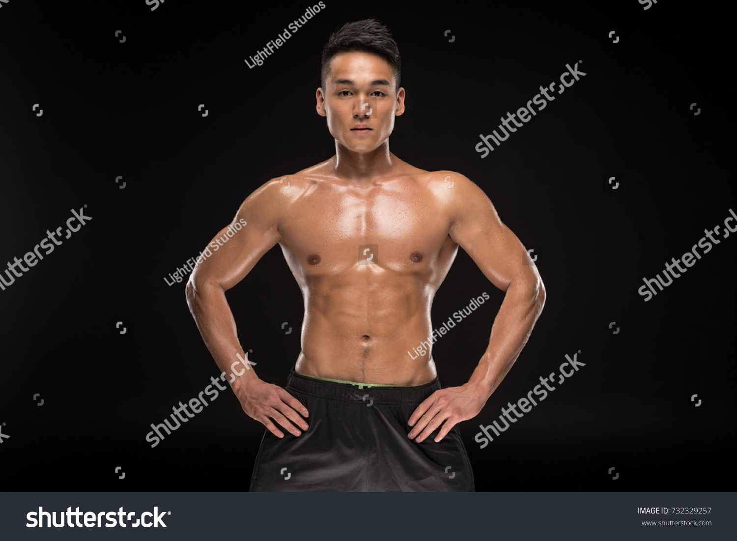 shirtless muscular asian man standing with hands on waist and looking at camera isolated on black