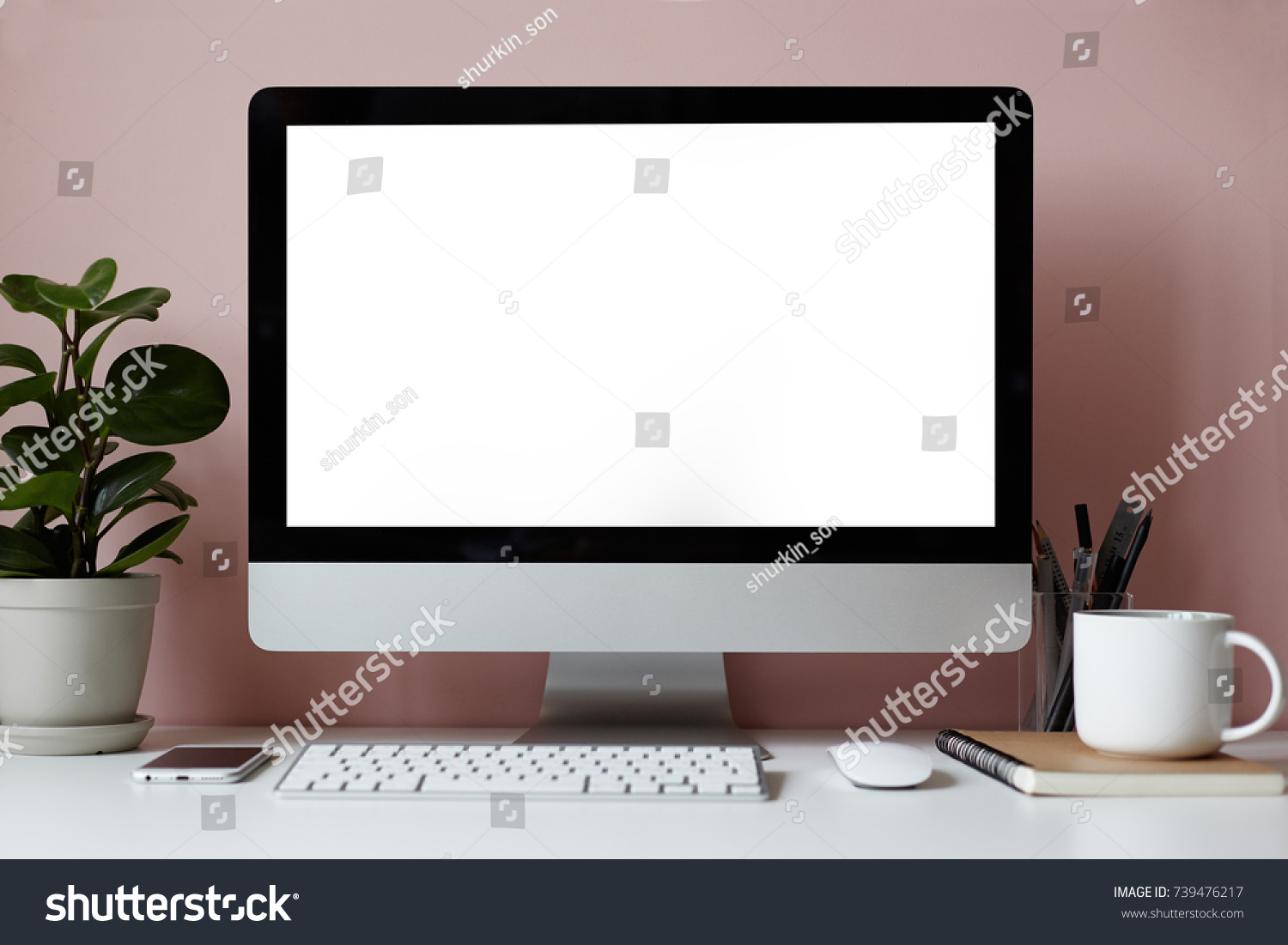Mock up of white desktop with electronic devices stationary items cup of tea copybook and decorative green plant over pinkish wall. Minimalistic modern workplace of student or freelancer