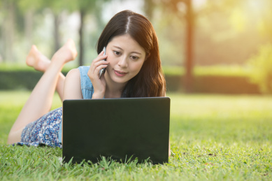 美丽的亚洲女子在户外公园使用电脑在草地上。大自然户外背景。人才和技术概念