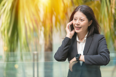 年轻的女商人的电话，望着远处的户外办公，检查智能手表，而在移动电话交谈。美丽的混血亚洲中国。