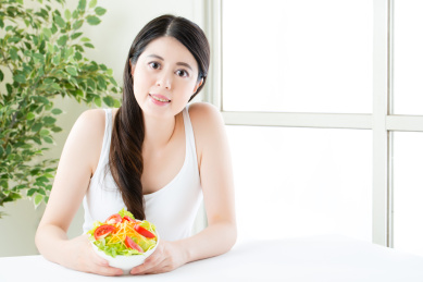 迷人的亚洲女子微笑展示沙拉，健康食品概念室内背景