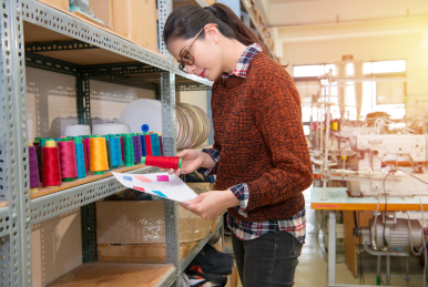 认真成功的设计师女子站在五颜六色的卷轴线程柜前，与时尚服装缝纫工作室纸样检查选择红色。