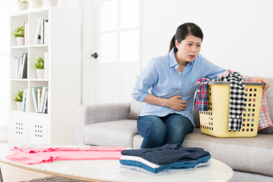 美丽不幸的女人坐在客厅的沙发沙发上有许多凌乱的家庭服装，当她月经痛时不舒服的感觉。