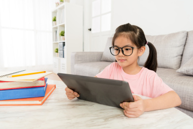 有吸引力的年轻女性的孩子的孩子在家里坐在客厅里，并使用移动数字平板电脑观看在线视频。