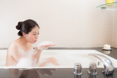 漂亮迷人的女人坐在浴缸洗澡，吹泡泡放松。