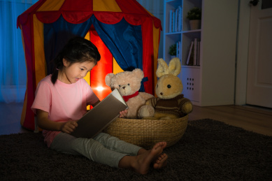 美丽可爱的孩子坐在孩子帐篷前和睡前在晚上拿着漫画书讲的故事在她的卧室里最喜欢的玩具。