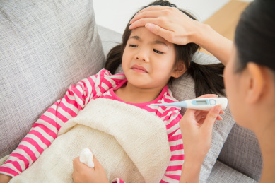 可爱的小亚洲女孩是生病躺在沙发床的母亲检查温度计和感人的女儿在家里客厅的额头。家庭活动的概念。