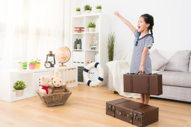 开朗可爱的小女孩穿着旅客水手服装，手持行李箱的行李站在木地板准备前往。