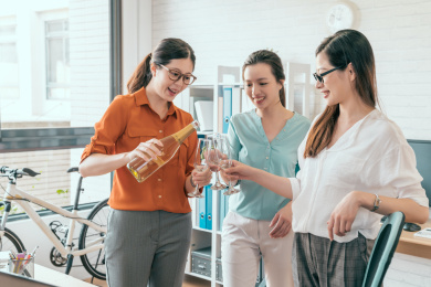 快乐的女商人拿着香槟笛子和站立时接近对方室内微笑集团。我们得到了一个合同的概念。