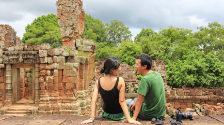 年轻亚裔情侣坐在柬埔寨吴哥窟遗迹的平台上发自内心的互相开心大笑