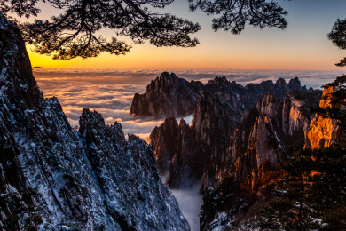 中国安徽黄山景区冬日雪后放晴，夕阳映照山崖云雾飘渺宛若仙境