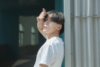 单手遮挡阳光的亚裔年轻男人侧身人像看镜头