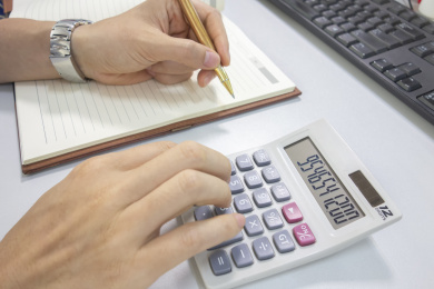 办公桌上拿着笔的手旁放着计算器